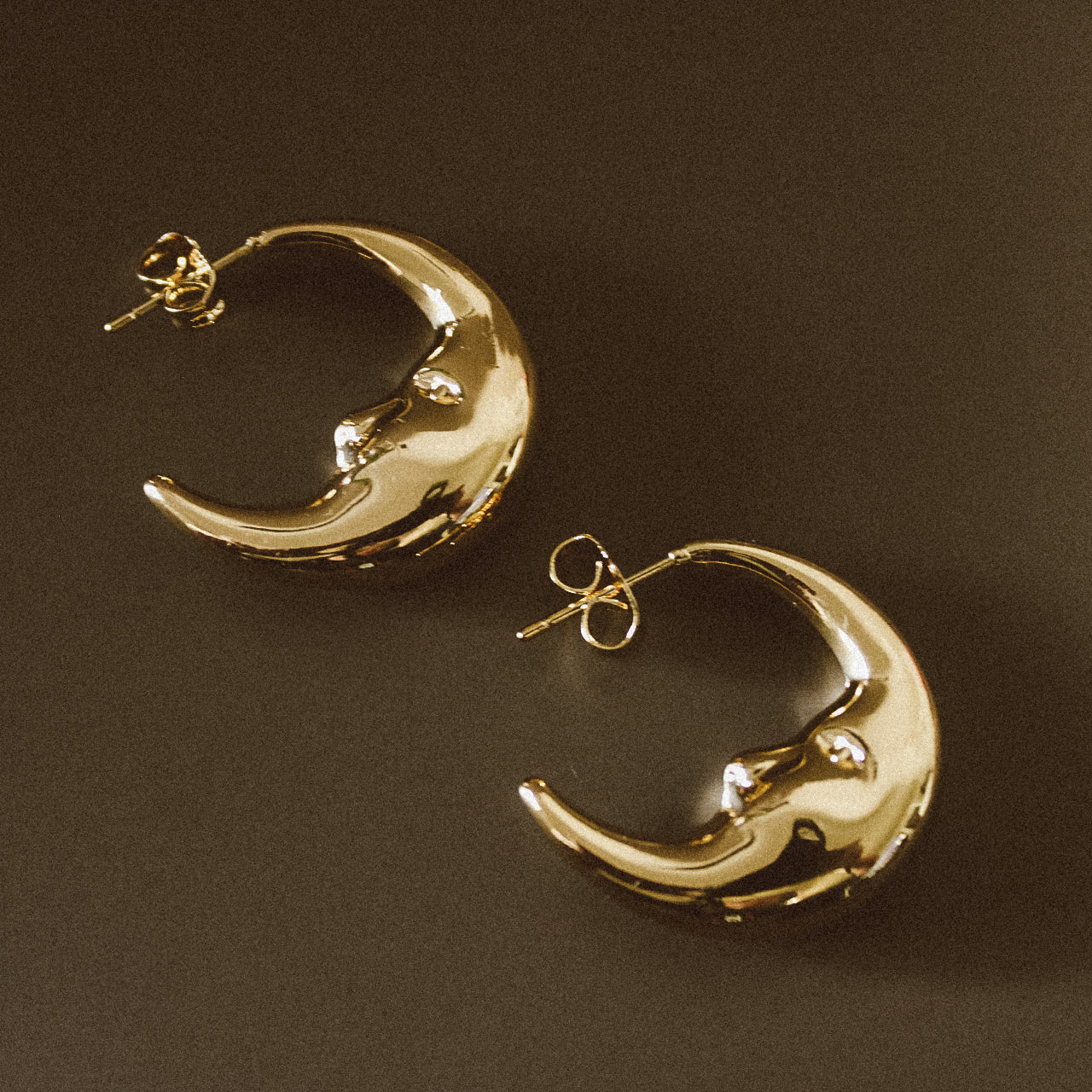 Gold crescent moon earrings on a dark brown background