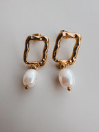 Gold hoop earrings with pearl drops on a light gray background