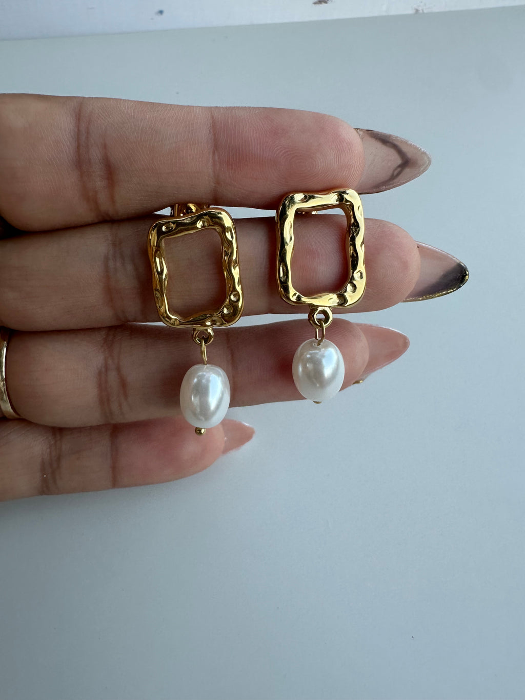 Gold earrings with pearl drops held between fingers on a white background