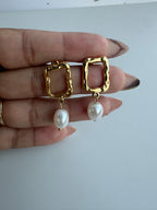 Gold earrings with pearl drops held between fingers on a white background