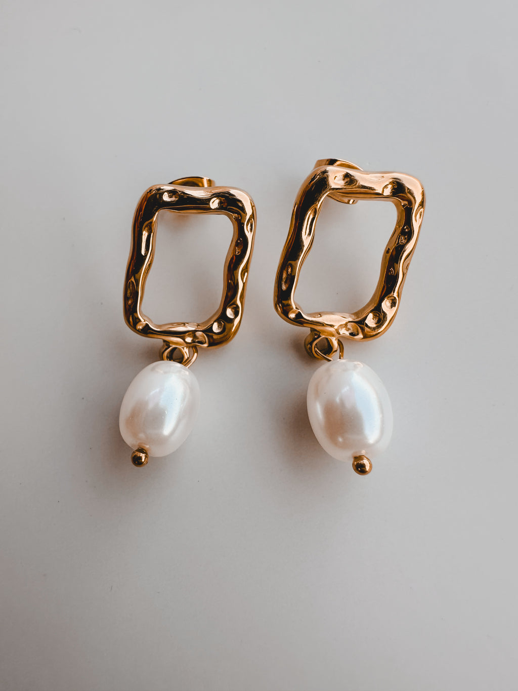 Gold hoop earrings with pearl drops on a light gray background