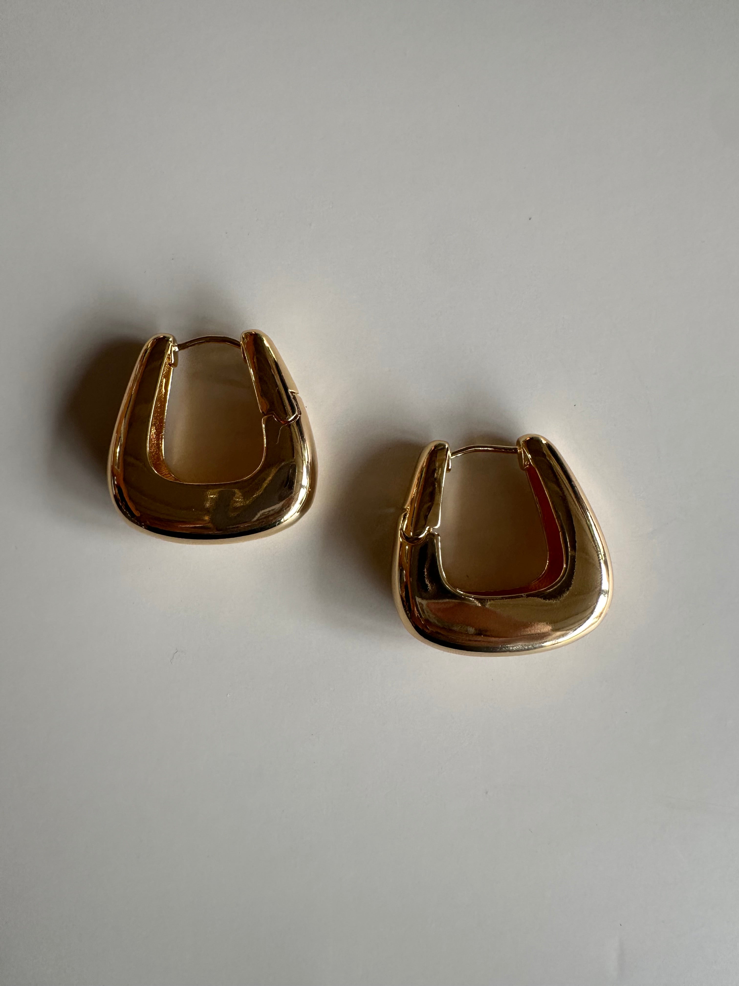 Two gold hoop earrings on a light gray background