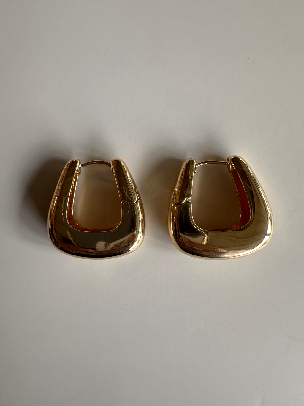 Two gold hoop earrings on a light gray background