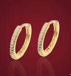 Gold hoop earrings with embedded stones on a red background