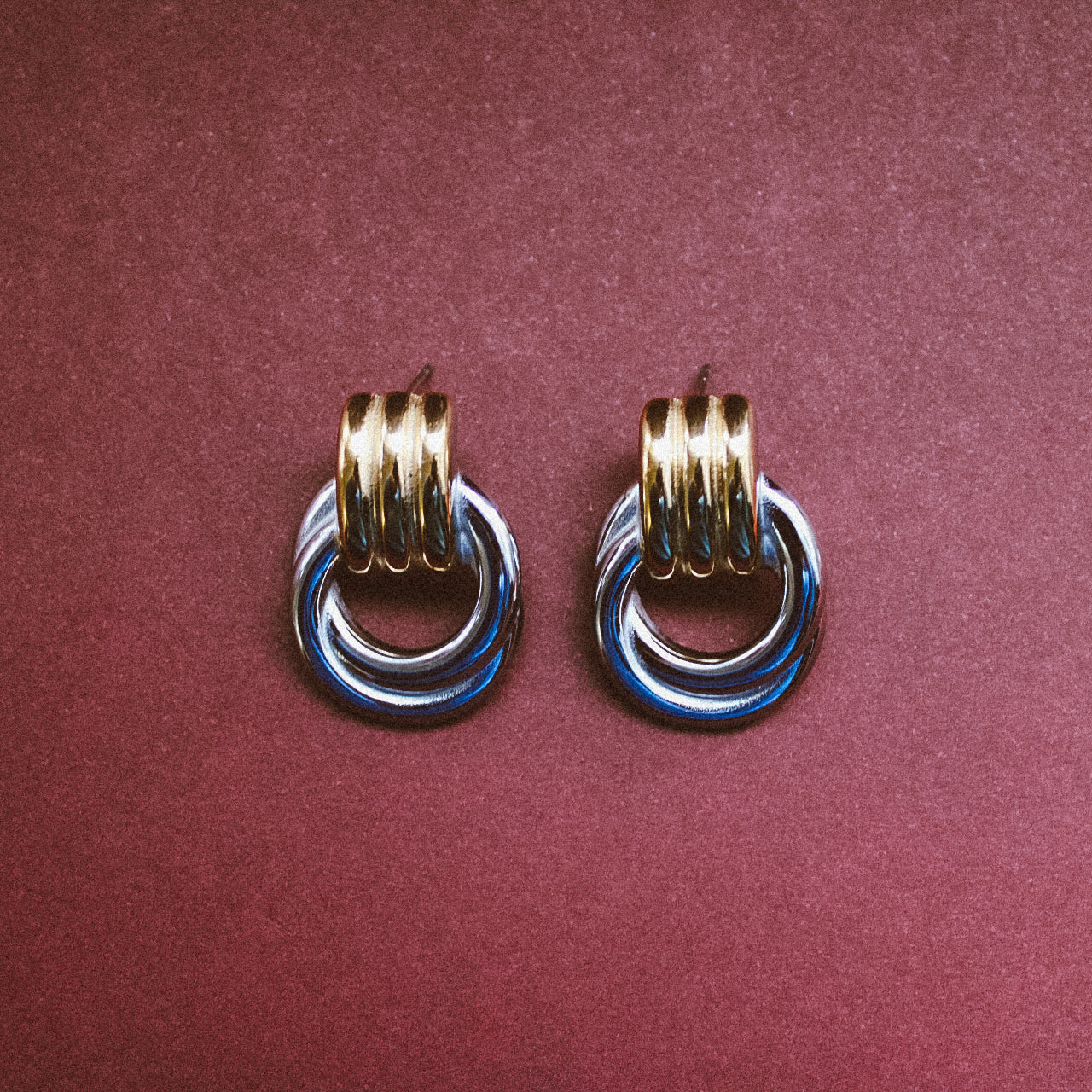 Bold Statement Stud Earrings Two Tone in a maroon background

