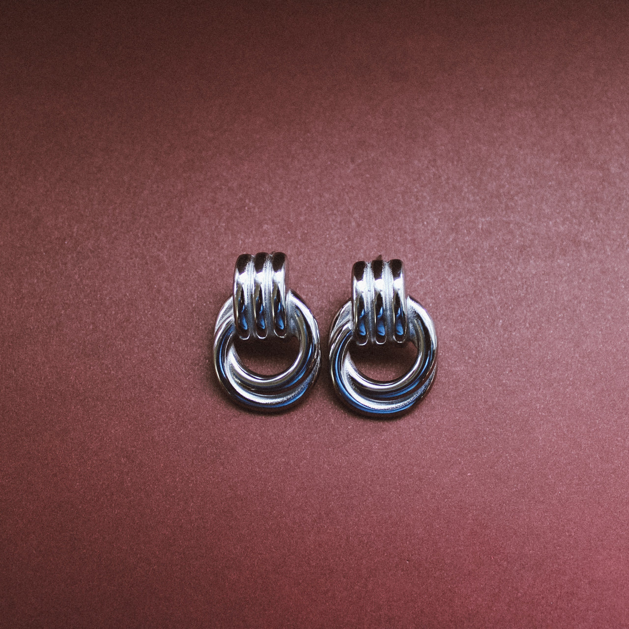 Pair of silver hoop stud earrings on a maroon background