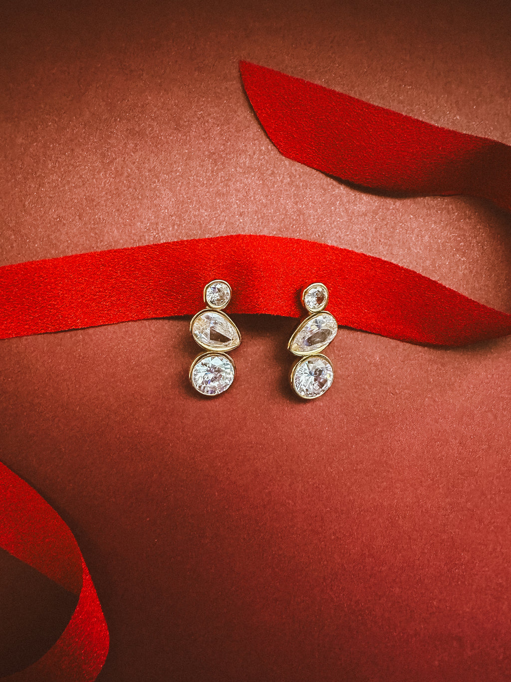 bezel drop earrings on a dark red background